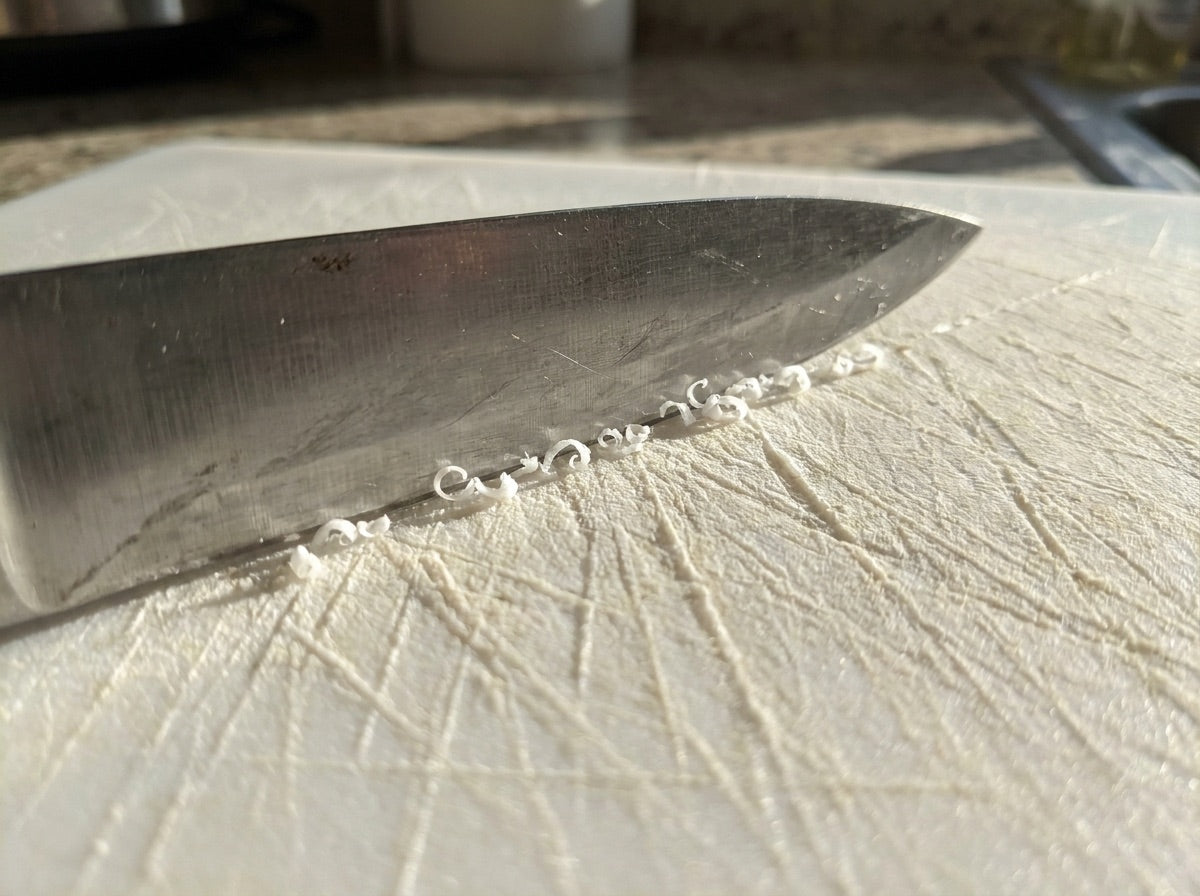 Knife shedding plastic shavings on a scarred cutting board
